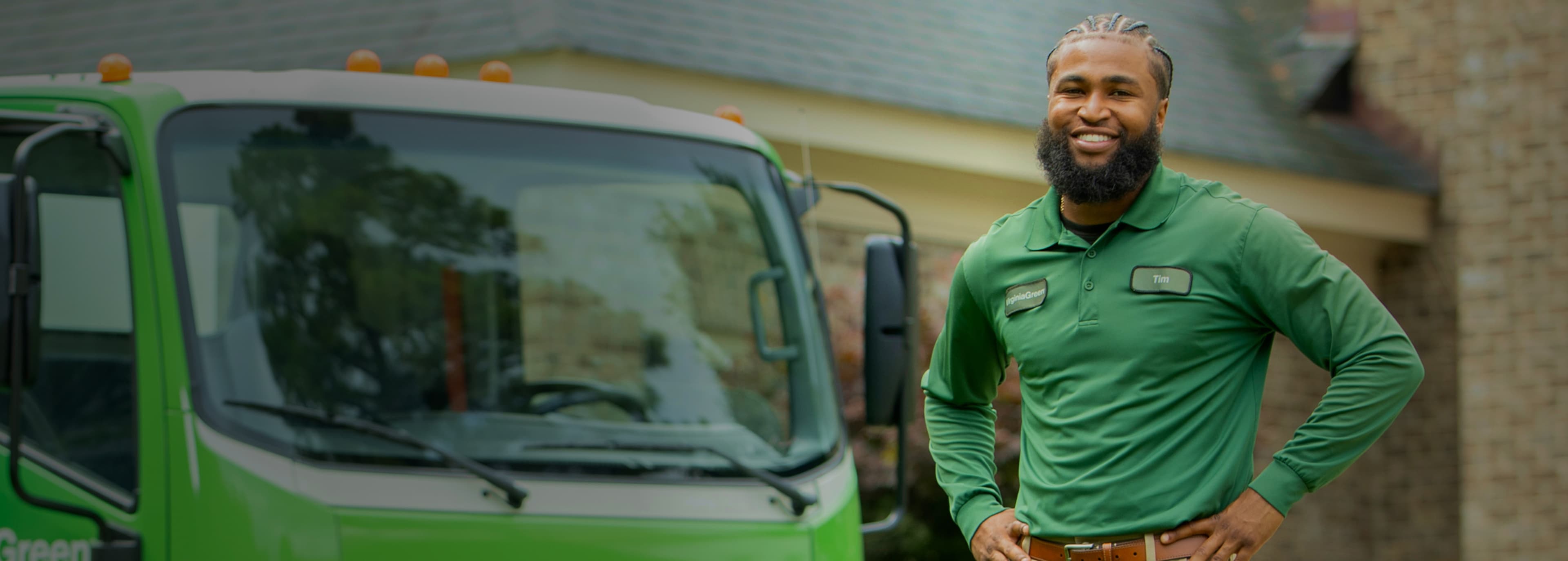 Virginia Green lawn care technician standing in front of a Virginia Green service truck outside a customer's home