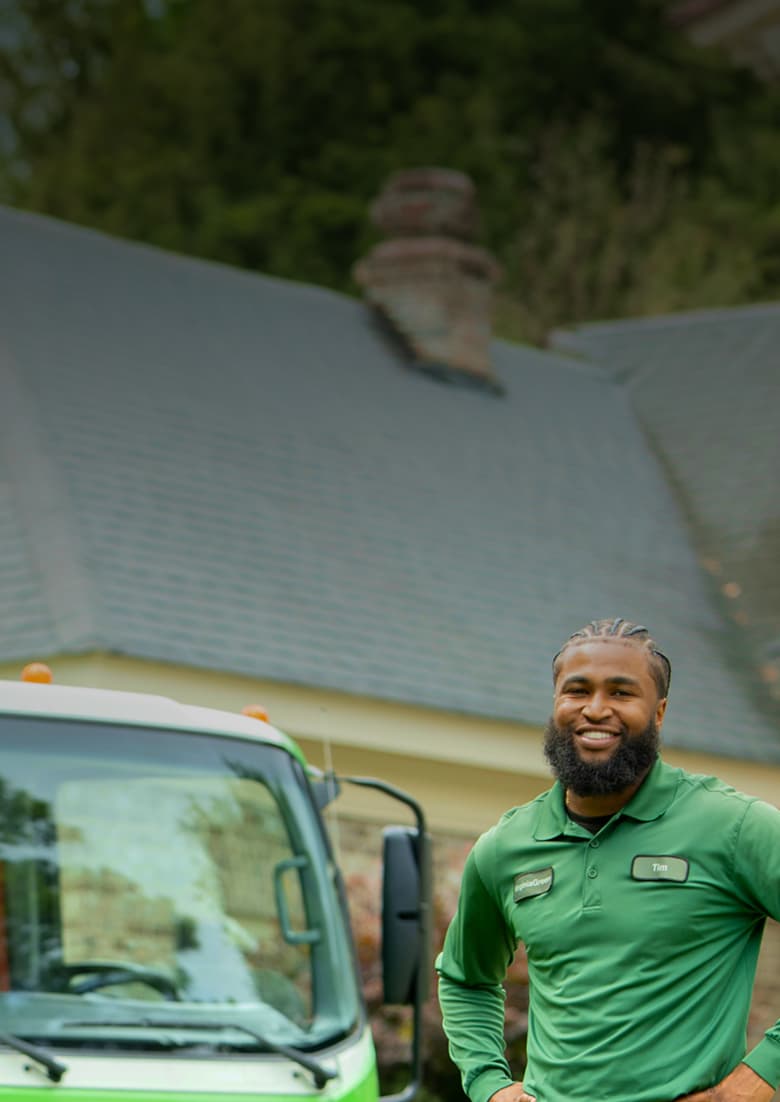 Virginia Green lawn care technician standing in front of a Virginia Green service truck outside a customer's home