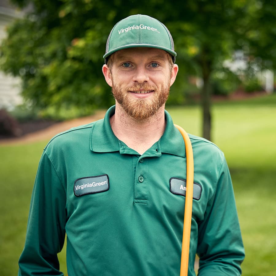 Virginia Green technician in a branded cap and polo standing on a treated lawn